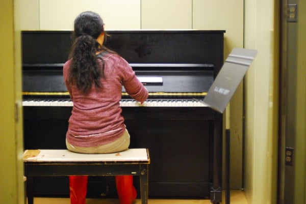 Girl sits on a bench in front of a piano.