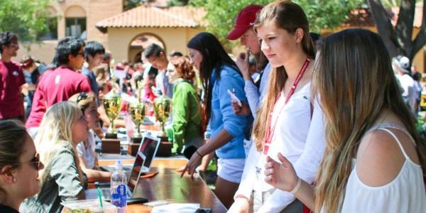 Students gather in front of wooden folding tables, wearing lanyards around their neck to discuss campus clubs during Admit weekend in 2015