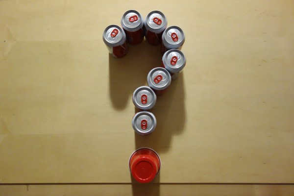 A series of beer cans, and a red solo cup arranged in the shape of a question mark.