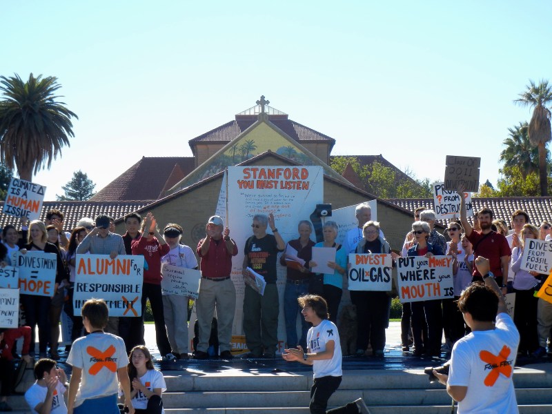Protestors stand in front of Memorial Church, wearing white t-shirts with orange X's and holding orange painted signs encouraging fossil fuel divestment.