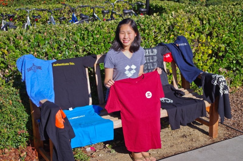 Olivia Wu '16 with a portion of the free T-shirts she has received from startups at career fairs. (ALLISON HARMAN/The Stanford Daily)