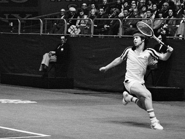 Black and white image of John McEnroe on a tennis court with his racket poised.