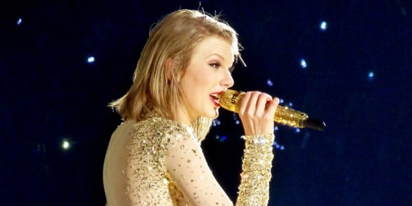 Taylor Swift, a prominent singer and songwriter, performs on stage holding a microphone.