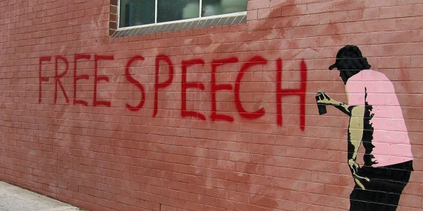 Graphic of a person spray painting "Free Speech" in red on a brick wall.