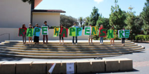Student protestors stand in White Plaza, with each student holding a letter spelling out "Rape Happens Here."