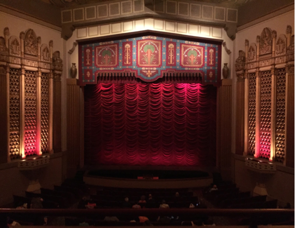 An ornate stage with a rippled bright red curtain.