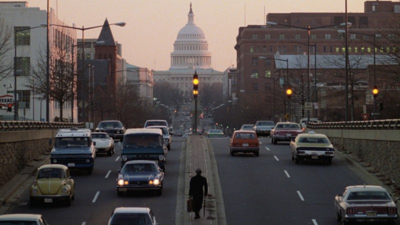 Capitol Hill viewed behind a street with cars and people at dawn.
