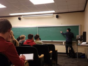 An instructor writing on a chalkboard in a lecture hall.