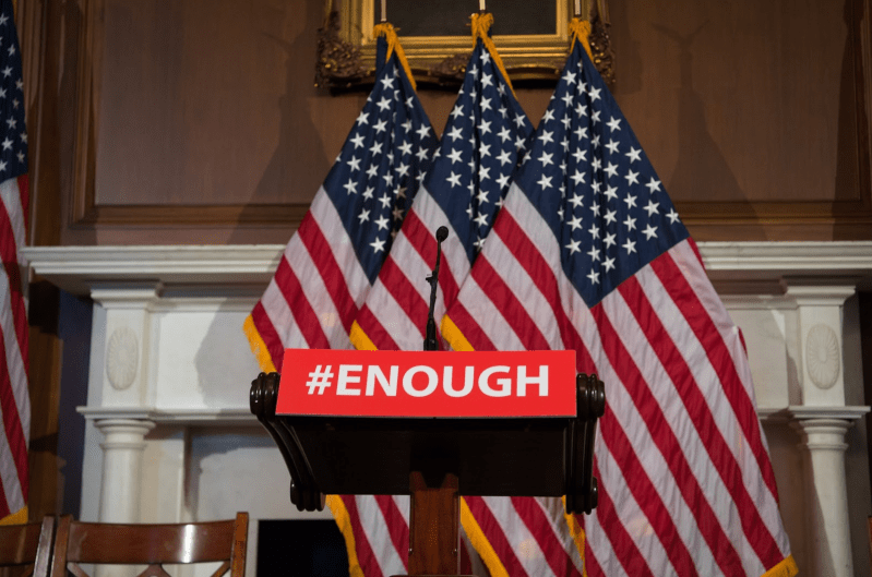 Three American flags hanging with the word "#ENOUGH" written across them.