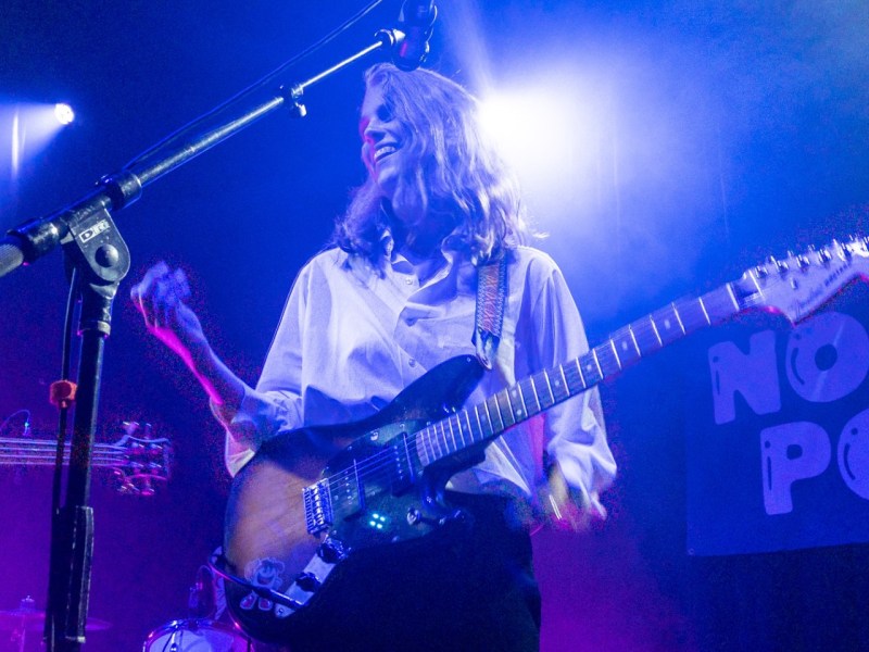 A beaming Marika Hackman stands bathed in moody purple lighting with an electric guitar slung over her shoulder. (Photo: Anupriya Dwivedi).