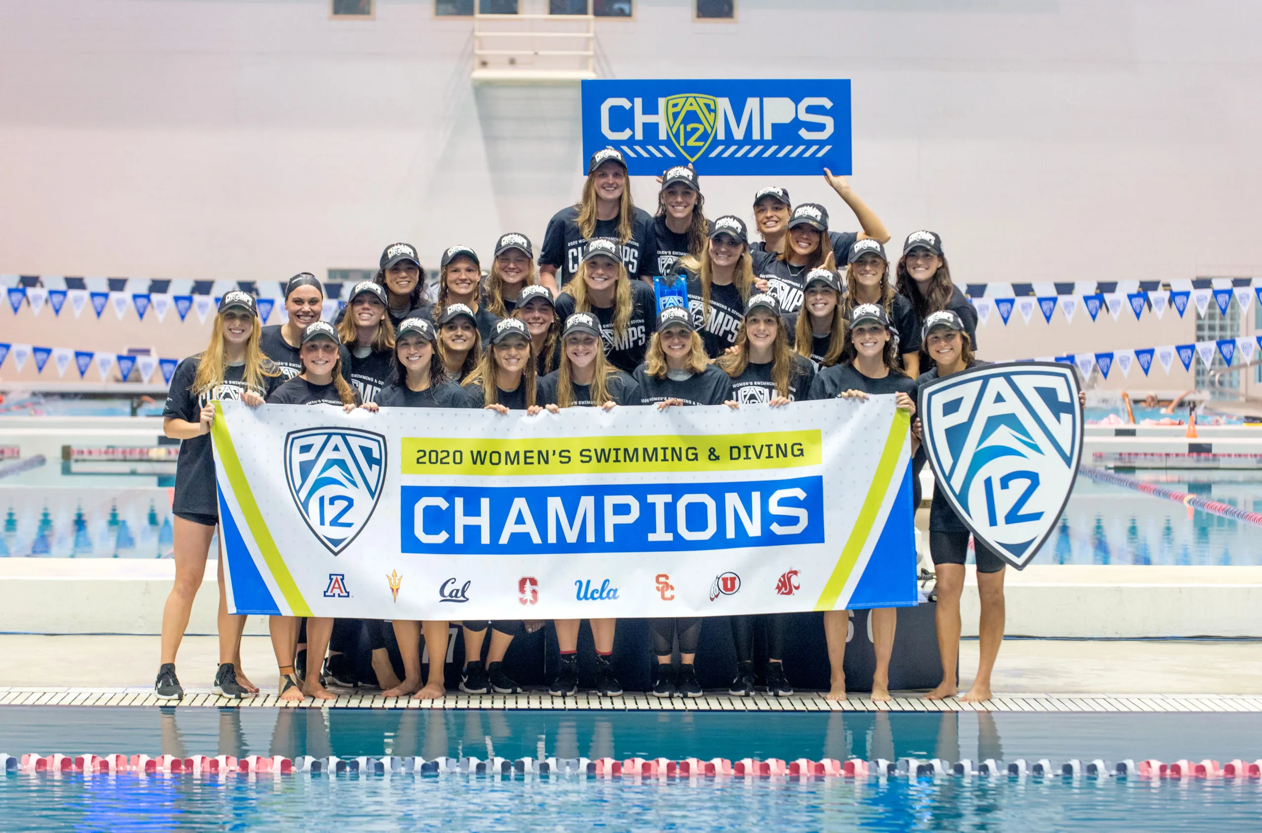 The women's swimming and diving team stands at the podium and holds up its Pac-12 title banner.