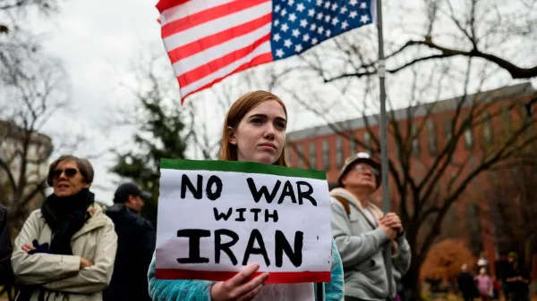 A woman stands with a "No War with Iran" poster at a protest