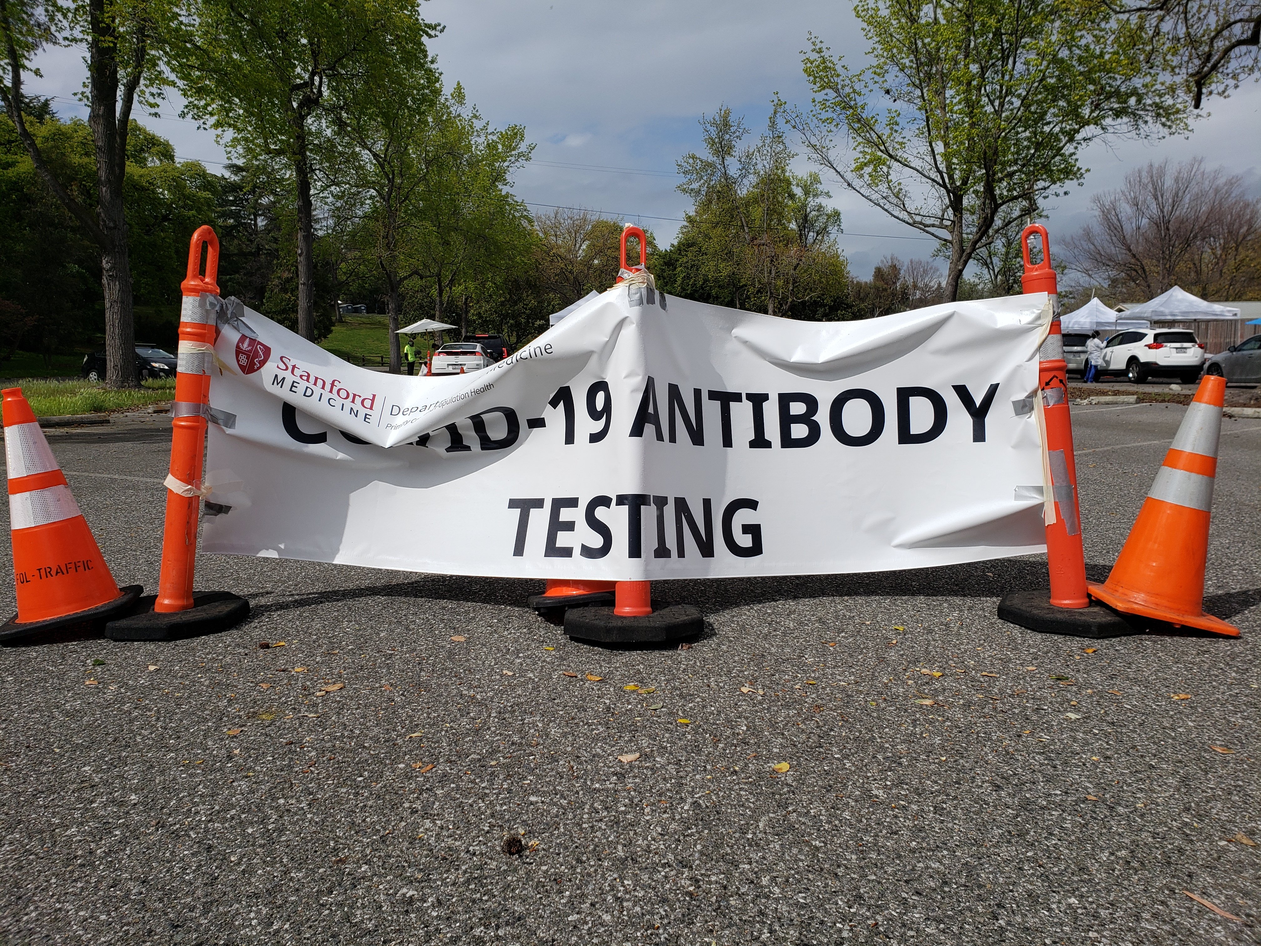 A sign directing people to 'COVID-19 antibody testing' is attached to traffic cones in a parking lot.
