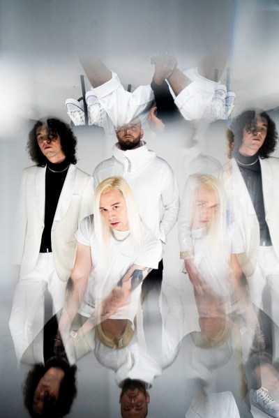 The three band members are dressed in mostly white clothing. Reflections of them are scattered throughout the image.