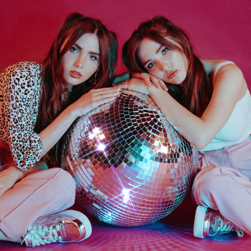 Two twin sisters lean on either side of a disco ball.