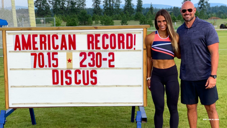 Valarie Allman stands next to a board with "American Record! 70.15 - 230.2 Discus."