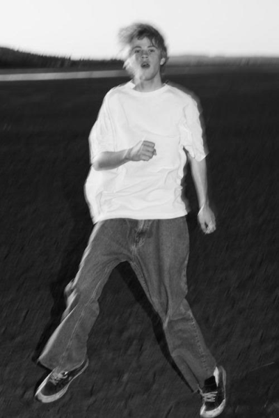 A black and white photo of Jimi Somewhere, who is wearing a baggy white T-shirt and jeans. The image is stylistically blurred.