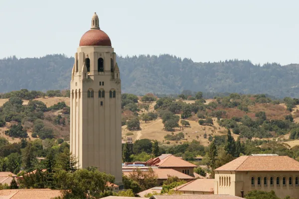 Hoover Tower above Stanford campus in front of green hills and grey sky.