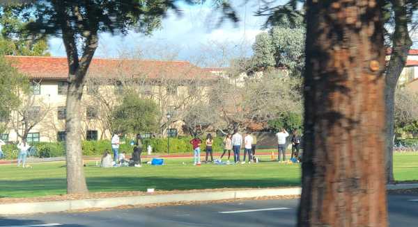 Students gather outdoors on Wilbur Field, some without masks. (Photo: The Stanford Daily)