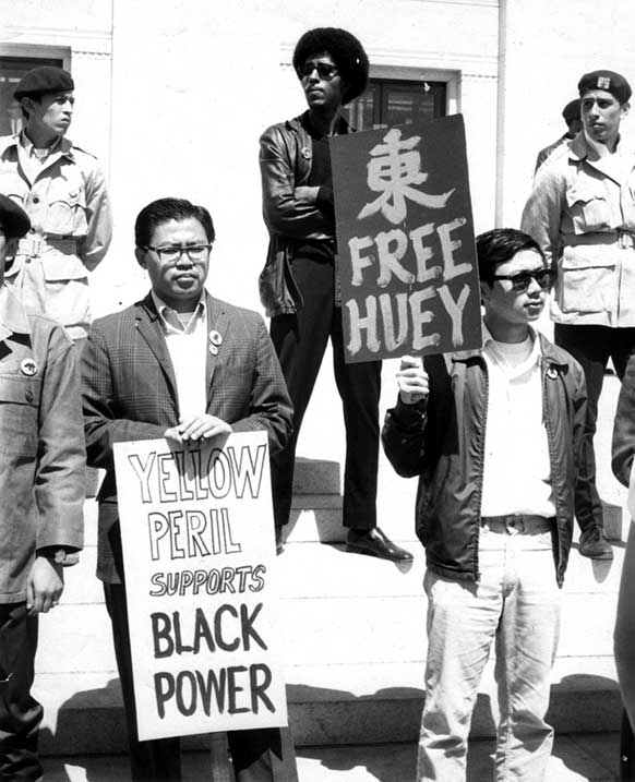 Black and Asian demonstrators stand holding signs: "Yellow Peril Supports Black Power" and "Free Huey"