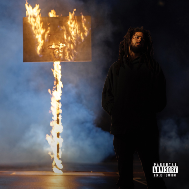 J. Cole standing in front of a burning sign