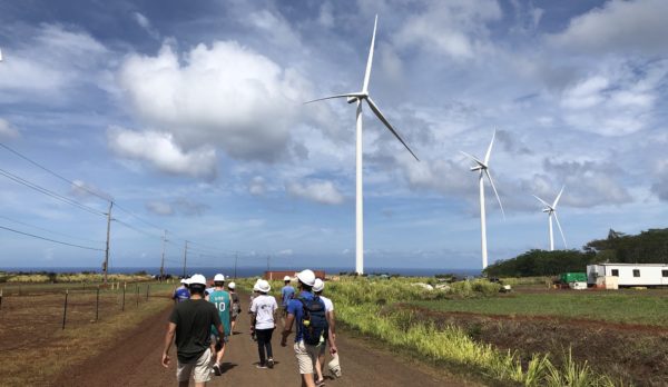 Students walk on a dirt path with windmills in the background