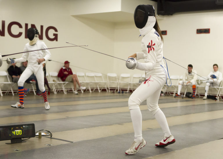 Former Stanford fencer Vivian Kong, pictured in the foreground, stands on a fencing mat ready to begin a match.