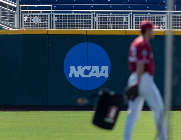 NCAA logo is shown on the field in a blue circle. A baseball player stands out of focus.