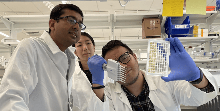 Three scientists. One is holding lab equipment.