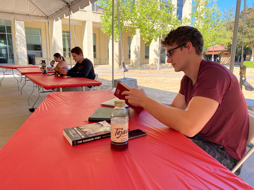 Students read their notes and books, sitting outside at tables covered in red table cloths during their in-person class this summer.