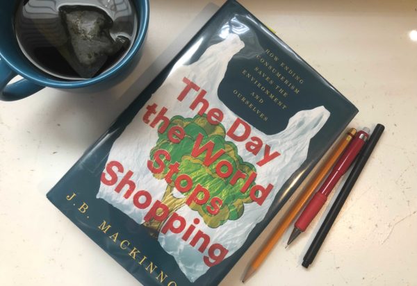 "The Day the World Stops Shopping" is on a table, surrounded by a mug and writing utensils.