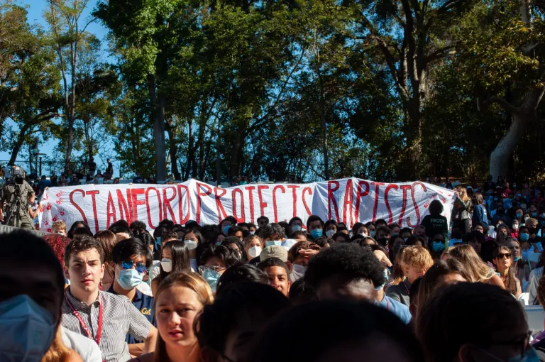 Sophomores carry a banner that reads "Stanford Protects Rapists" behind a section of seated Sophomore students at Convocation.