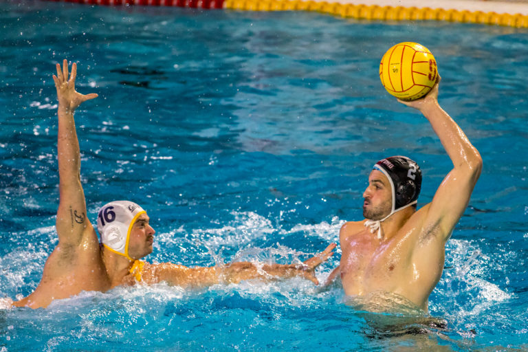 Men's water polo player Tyler Abrahamson rises up from the water to make a pass with a water polo ball.