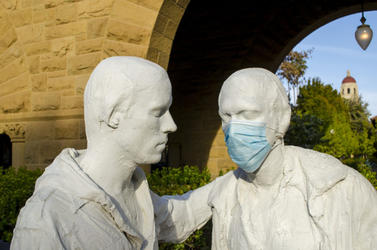 A photo of two statues on stanford's campus with one wearing a blue surgical mask