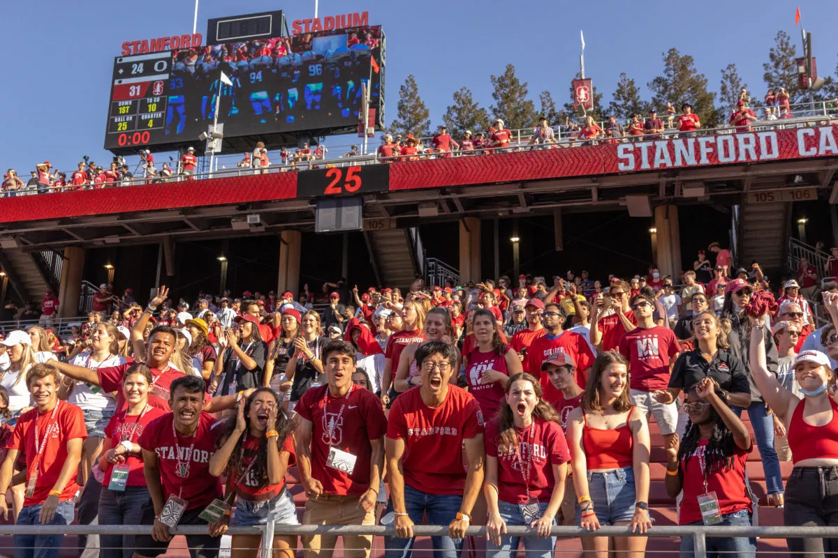 A sea of students in the stadium stands wearing red shirts screaming at the field. 