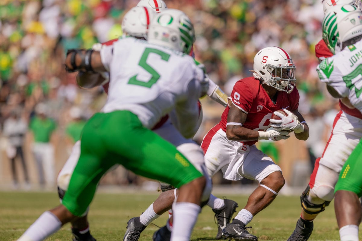Junior running back Nathaniel Peat charging to the right with the ball in hand. In the foreground, several Cardinal football players hold back the Ducks football players.