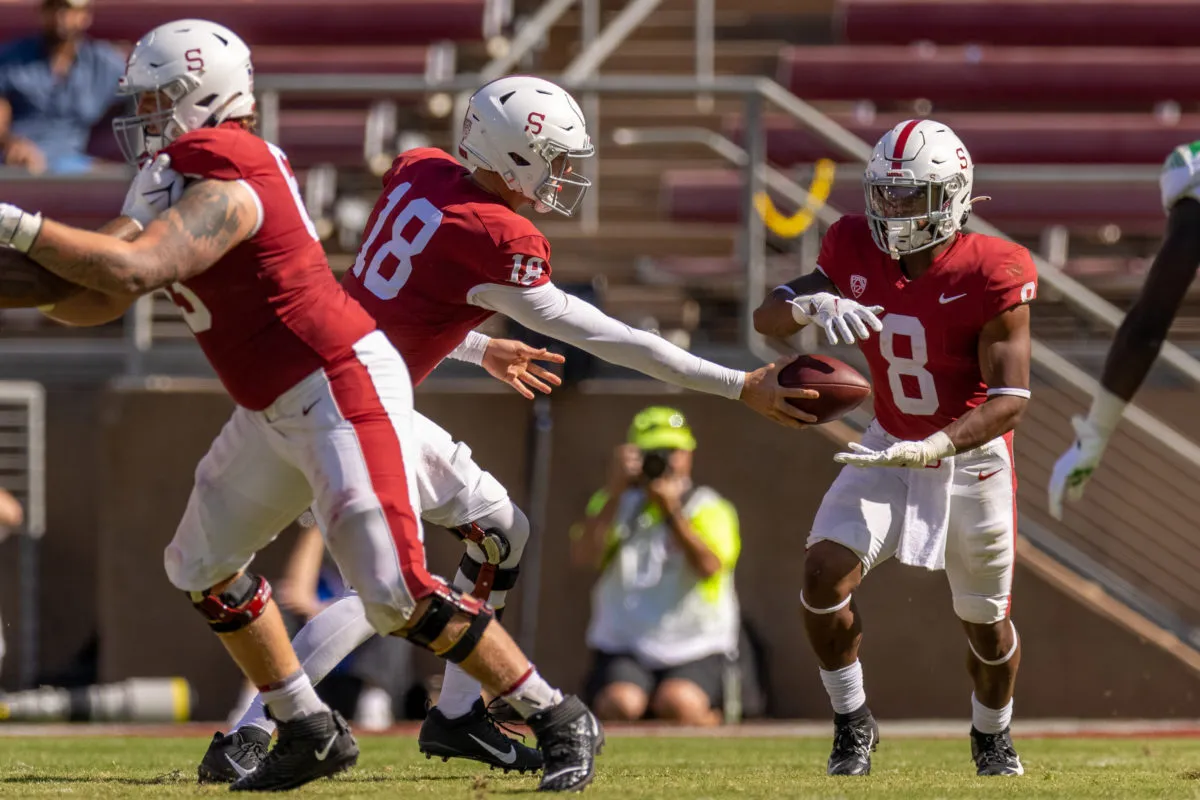 Sophomore quarterback Tanner McKee hands the ball off to junior running back Nathaniel Peat. Another Stanford football player holds back an unseen Oregon player.
