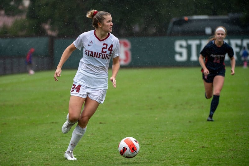 A soccer player in a Stanford jersey dribbles a soccer ball up a soccer field.