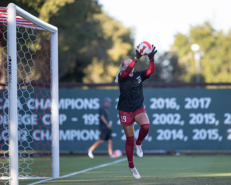 Goalkeeper Katie Meyer jumps up to save a ball in front of a soccer net.