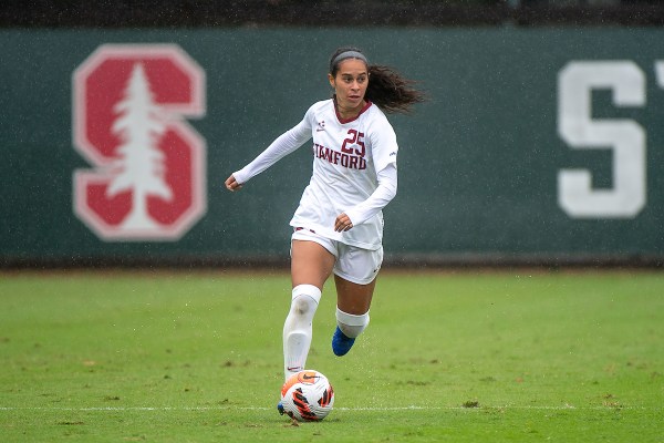 A women's soccer player in a Stanford jersey dribbles a soccer ball down a soccer pitch.