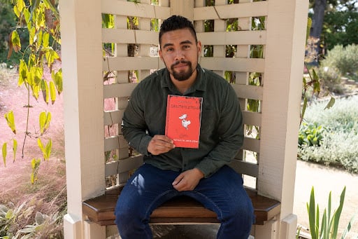 Poet Antonio de Jesús López poses with his book "Gentefication" underneath a trellace