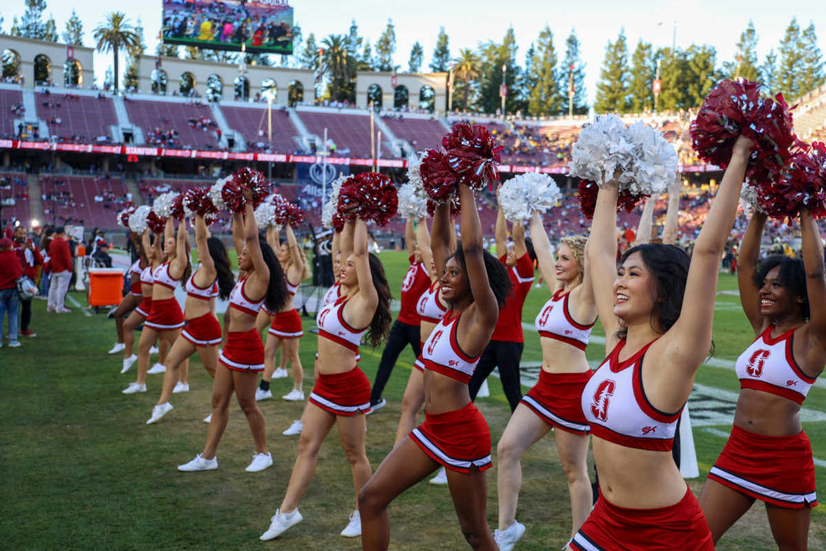 Line of Stanford cheerleaders holding pom-poms, smiling towards bleachers