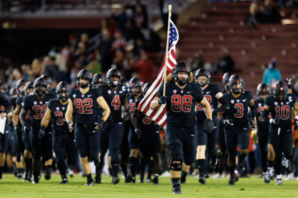 Fifth-year tight end and defensive end Tucker Fisk carries the American flag and leads the team through the tunnel at Stanford stadium.