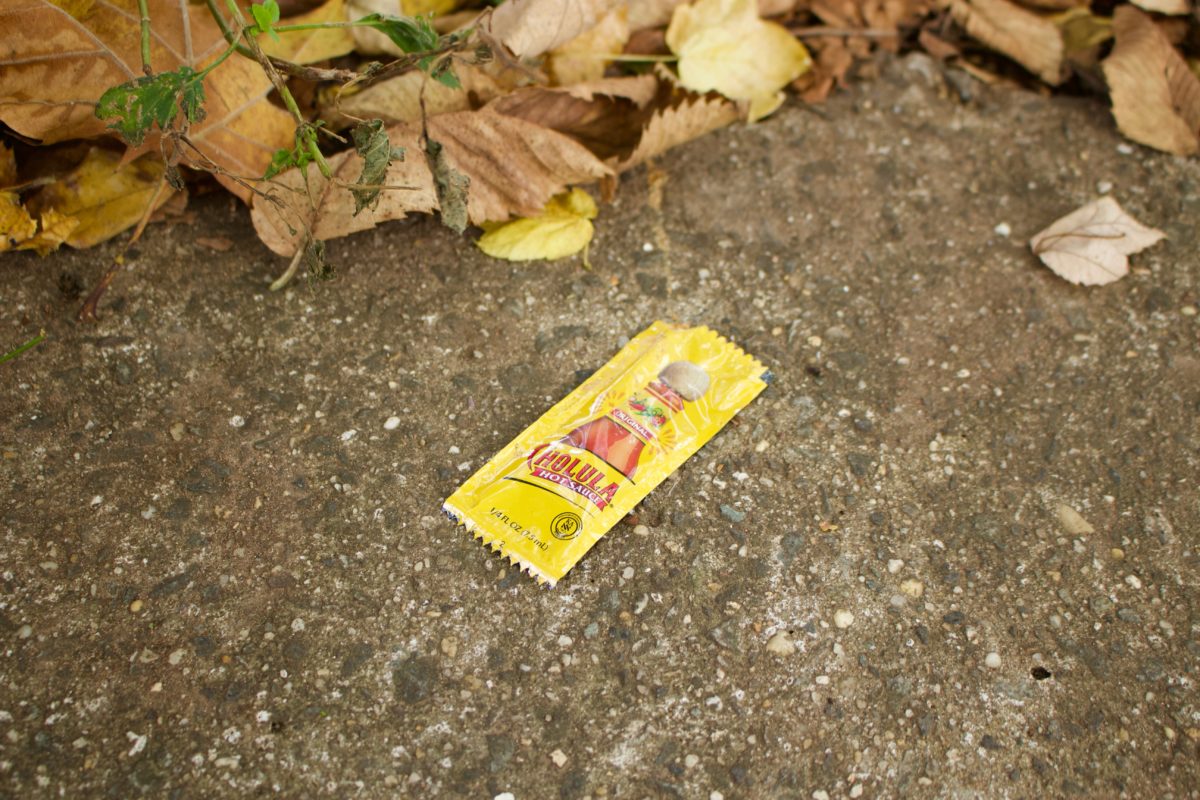 A hot sauce packer on the ground by some leaves.