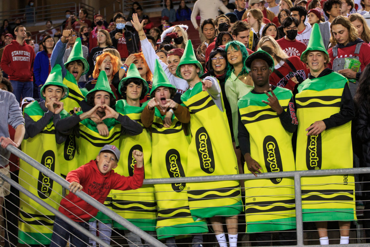 Picture of a crowd of students dressed in Crayola and other Halloween costumes cheer and point at the camera. 