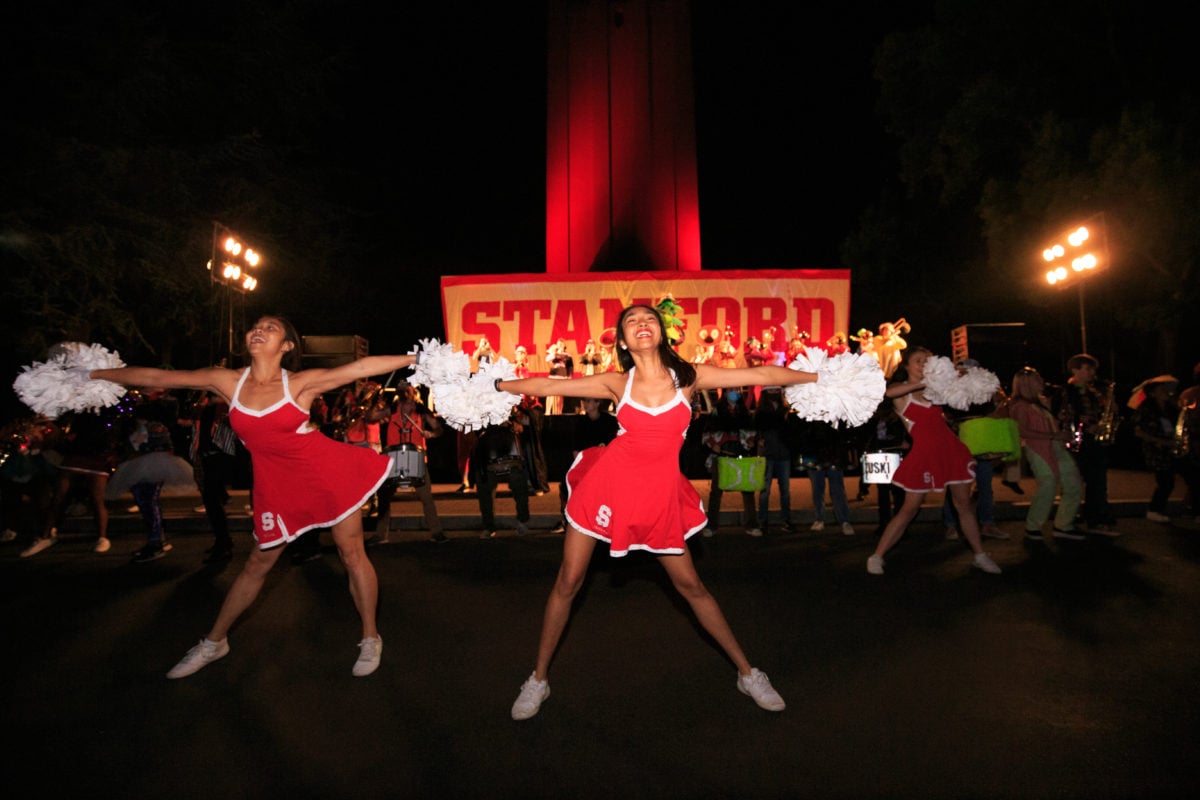 In the night, three Stanford dollies stand in front of a banner labeled "Stanford". Hoover Tower is lit red in the background.