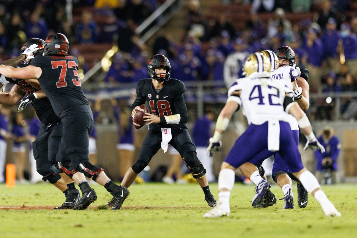 Stanford quarterback in the center holds the football while Washington defense rush towards him. 
