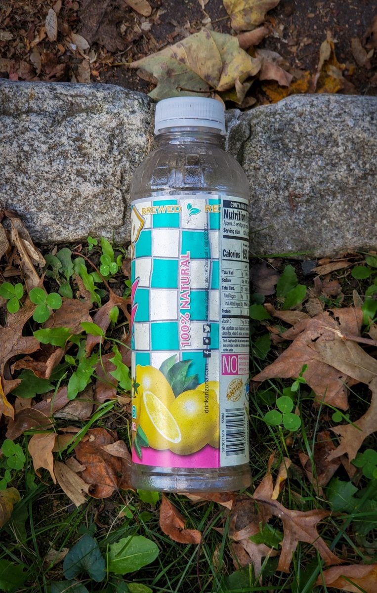 Arizona iced tea bottle on the grass by the sidewalk.