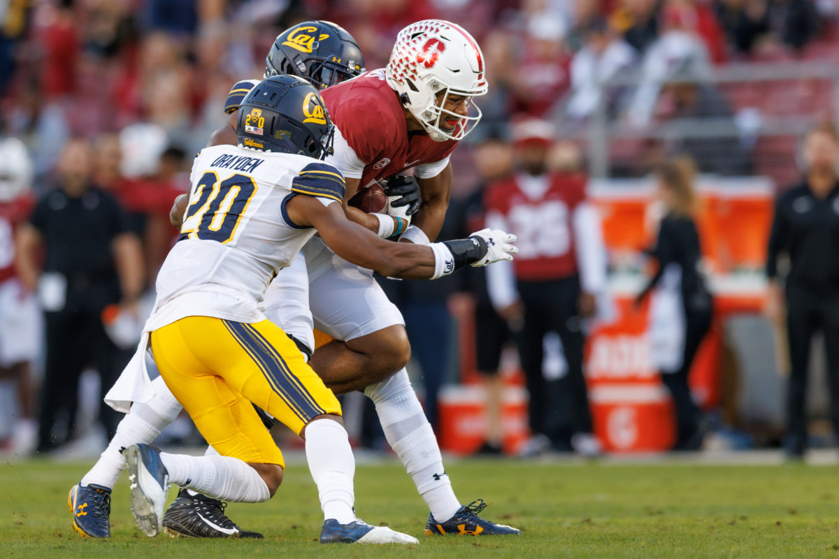 Stanford football player Elijah Higgins sandwiched on the field by two Cal defenders after a catch