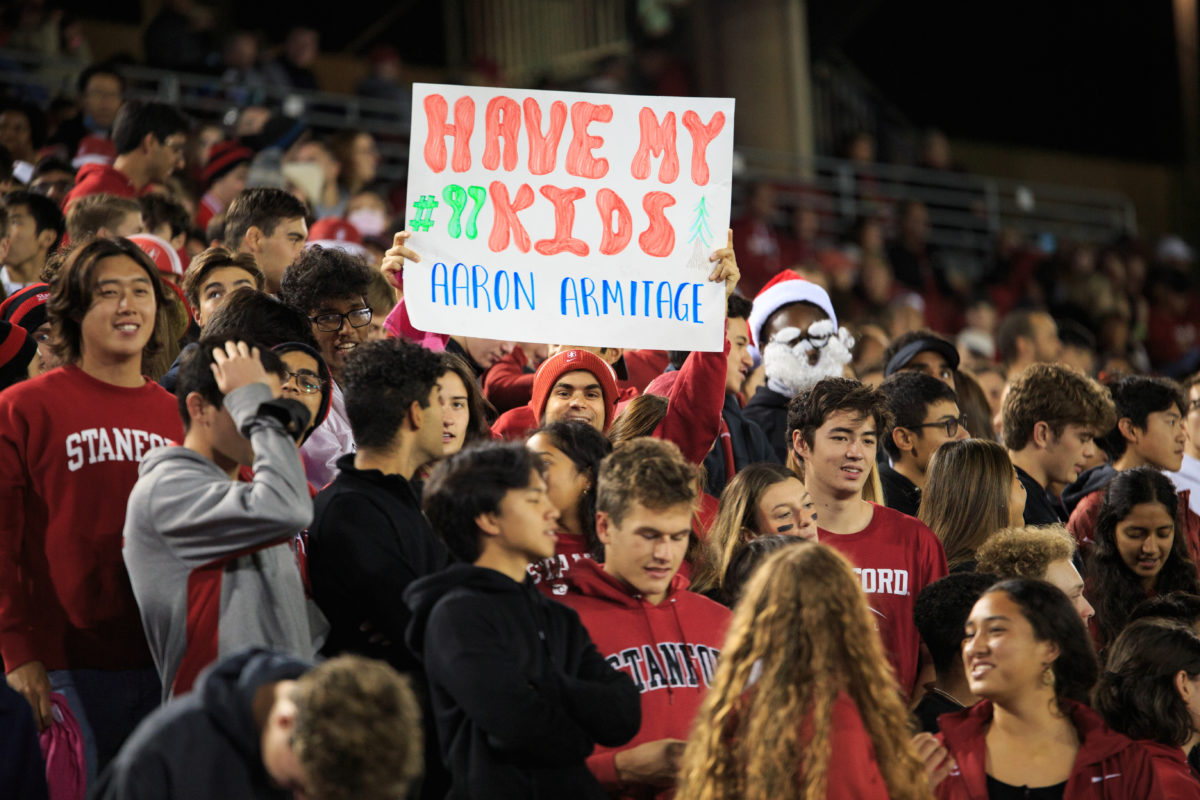 Crowd of students dressed in red Stanford merch, one of which is holding up a paper sign that reads "HAVE MY KIDS #97, Aaron Armitage". 